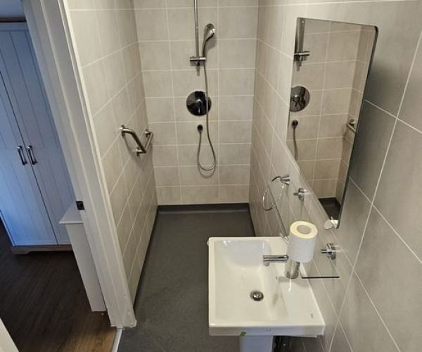 New accessible en-suite shower room with grab rails and basin in a care home bedroom